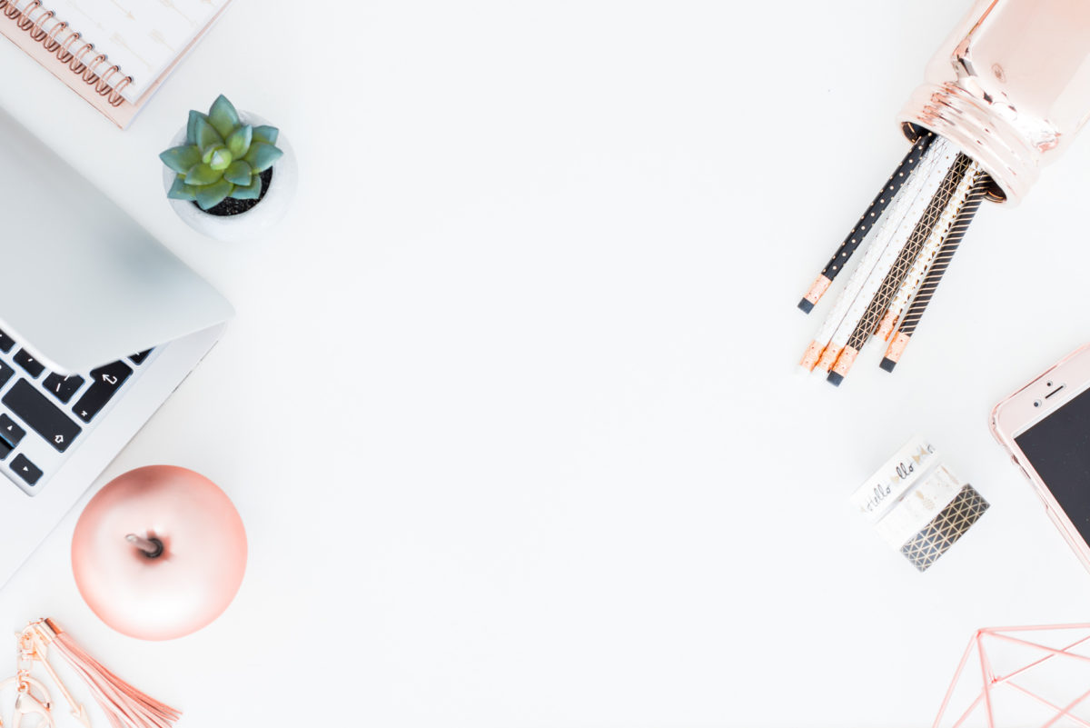 A white desktop with numerous rose gold office supplies, a silver computer and a green succulent. 